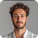 Portrait of a man with curly hair, beard, and mustache wearing a white shirt against a gray background.